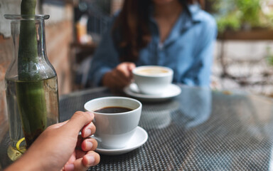 Closeup image of a young couple holding and drinking coffee together in cafe