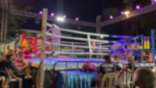 Blurred motion background youth amateur Muay Thai Boxing match break time red and blue corner with trainer. Thai boxing fighting on stage ringside view at night time outdoor arena spotlight