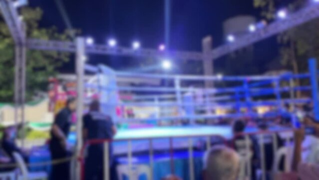 Blurred motion background youth amateur Muay Thai Boxing match red corner boxer enters the ring. Colorful outdoor arena spotlight at night