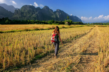 Fototapeta na wymiar Woman walking through harvested rice field in Vang Vieng, Laos