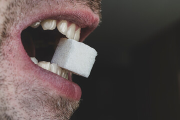 man bites a cube of white sugar with his teeth. The concept of harm to the health of teeth from...