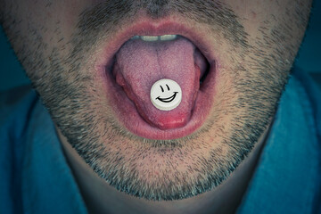 A pill with a synthetic drug on the tongue of a young man. smiley face on a white tablet. guy sucks...
