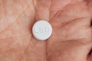 a white pill with LSD written on the palm of a man's hand. concept of drug addiction