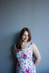 Young beautiful happy woman of European appearance in a dress against the background of a monochromatic gray wall