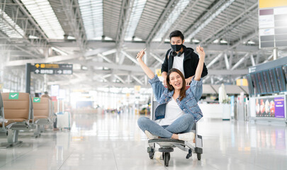 Young asian couple are happily waiting on a luggage trolley while waiting for a flight at airport...