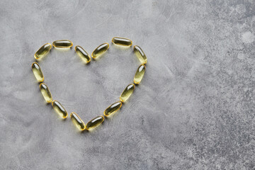 Fototapeta na wymiar Heart-shaped omega-3 capsules on a gray background. The concept of medicine and healthy living. Top view.