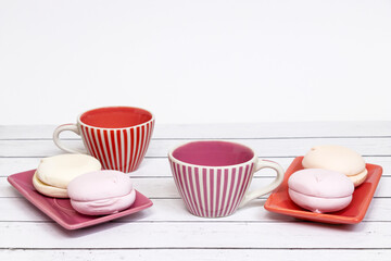 Sweet marshmallows of delicate pink color and two ceramic cups on a light wooden table. Close-up. Sweet breakfast for two.