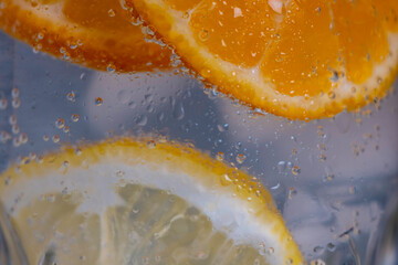 Fototapeta na wymiar Slices of orange and lemon in ice water, close-up, refreshing drink.
