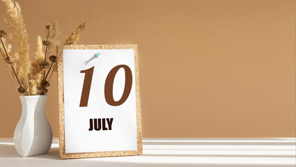 july 10. 10th day of month, calendar date.White vase with dead wood next to cork board with numbers. White-beige background with striped shadow. Concept of day of year, time planner, summer month