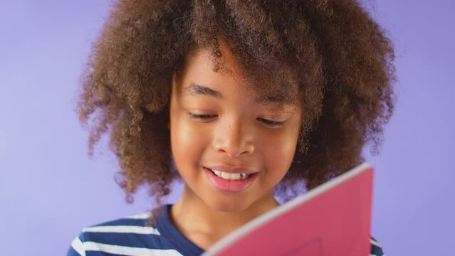 Studio Shot Of Young Boy Studying School Exercise Book Against Purple Background