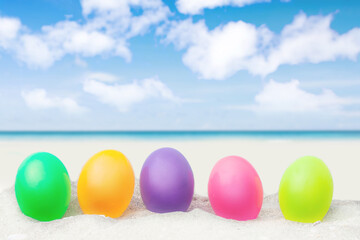 colorful eggs on white sand beach over blue sea background.