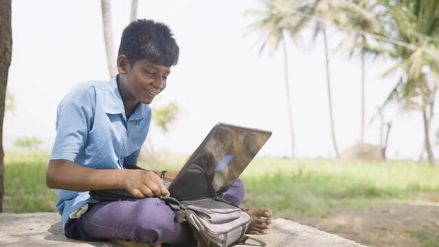 village school kid during online class using laptop near agriculture farmland - concept of education, distant e-learning and technology