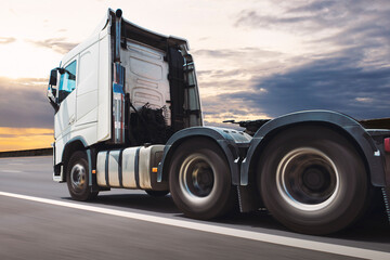 Semi Truck Driving on the Road with the Sunset Sky. Fast Spinning Wheels. Diesel Tractor Truck. Freight Truck Logistics Shipping Cargo Transport Concept.