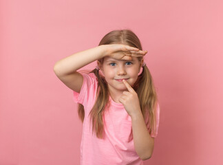 Little thinking smiling girl looking forward keeping palm on her forehead over pink background.  Searching concept.