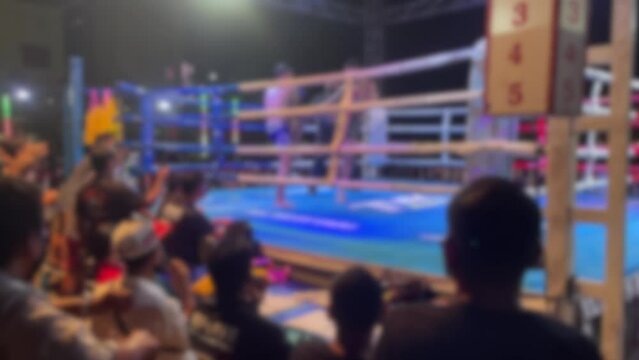Blurred motion background youth amateur Muay Thai Boxer punch, kick, knee and elbow on canvas outdoor boxing ring. Thai boxing fighting on stage with fan and trainer cheer on ringside night time