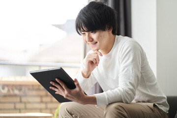 自宅のリビングでタブレットを使うアジア人男性