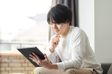 自宅のリビングでタブレットを使うアジア人男性