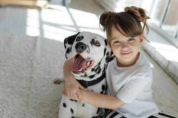 Child with a dog. A happy girl lies on a carpet with a Dalmatian dog. High quality photo