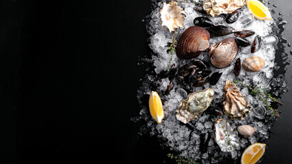 Raw oysters and mussels on ice on black slate. Fresh Clams in whole shells for cooking with seasonings on the table, top view and copy space © Andrey
