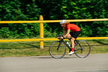 Fototapeta premium Redhead woman with curly hair in a helmet riding street racing bike on a road