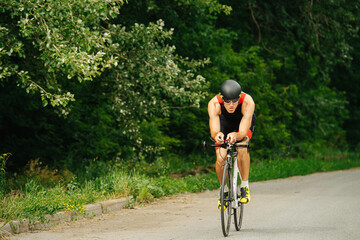 Obraz premium Muscular man riding his racing bike on a road through park with overgrown trees