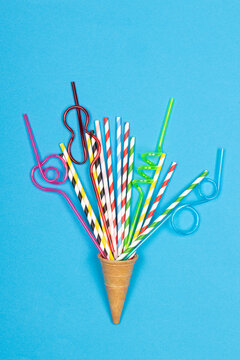 Ice cream cone with colorful drinking straws on blue background. Drinking cocktail party straws in waffle cone