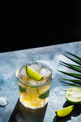 ice tea with ice cubes, lime, mint leaves in the glass on gray stone background