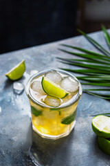 ice tea with ice cubes, lime, mint leaves in the glass with palm leaves on gray stone background