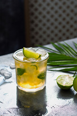 ice tea with ice cubes, lime, mint leaves in the glass with palm leaves on gray stone background
