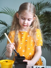 Little toddler girl planting seeds in the pots. Child helping to care for home plants. Home gardening, transplanting plants, seedlings