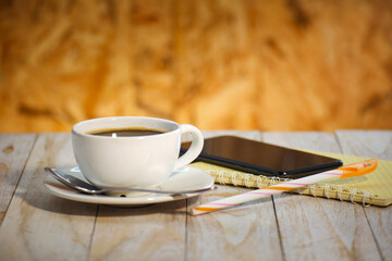 A hot cup of coffee, a notebook, a pen and a smartphone on the table.