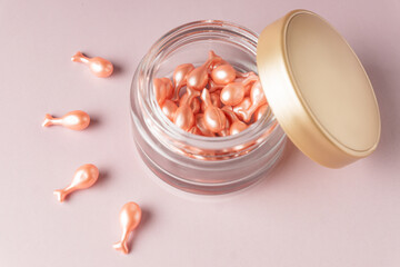 pink cosmetic capsules on pink background skattered out from a jar. Single dose serum or cream for...