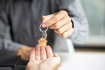 A home rental company employee is handing the house keys to a customer who has agreed to sign a...