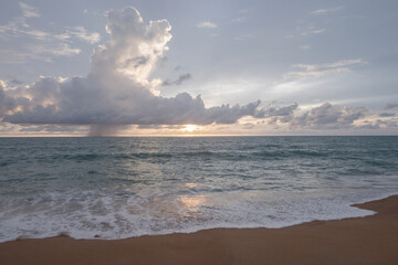 Cloudy afternoon and sunset with the sea and waves crashing on the sandy beach.