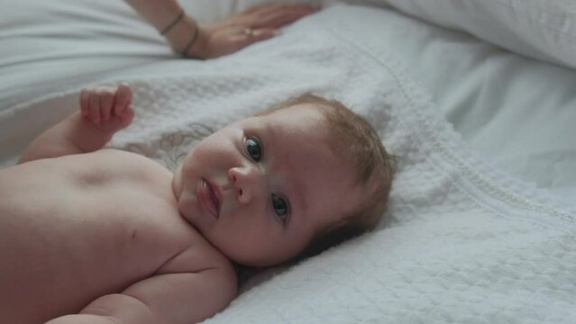 Portrait of a little newborn girl on a white sheet, taken in daylight. The child smiles and wonders