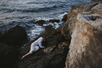 sensual woman in a secluded spot on a wild rocky coast in a white dress view from above