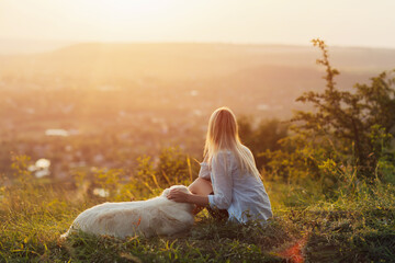 Fototapeta na wymiar A beautiful girl hugs her golden retriever on the mountain. Young woman with a dog at sunset.