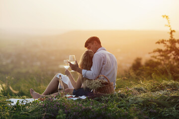 Beautiful young happy couple relaxing together on mountain at sunset with beautiful landscape on background.