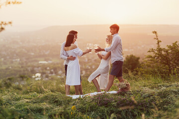 Beautiful happy people enjoy white wine on picnic date in beautiful setting at nature. Romantic getaway for friends.