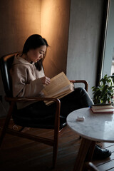 Shot of young asian female student sitting at table and writing on notebook. Young female student studying in cafe.