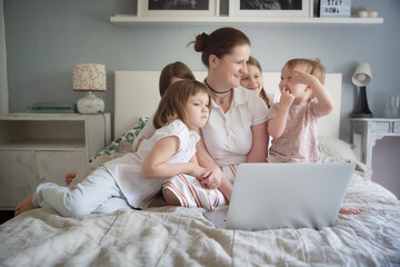 Mom and 4 children are looking at a laptop, watching a movie together. Mom freelancer working at...