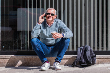 Related tourist man with backpack having coffee and using mobile phone