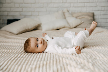 Fototapeta na wymiar 4 months old baby wearing white overall, lying on a soft blanket on bed at home, looking at camera.