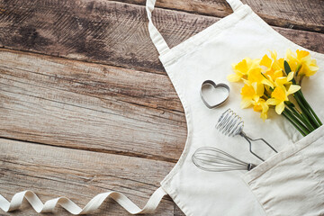 Apron and utensils baking desserts with bouquet of fresh daffodils on a wooden background. flat lay, top view