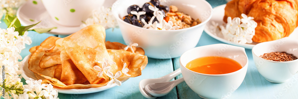 Wall mural Breakfast - crepes, muesli, croissant, tea, jam and a lilac on a blue wooden table. Spring background. Banner