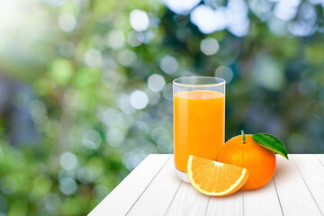 Glass of orange juice with fresh orange fruit on wood table with green nature blurred background.
