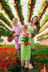 Grandmother, mother and daughter posing for photo while holding flowers in greenhouse.