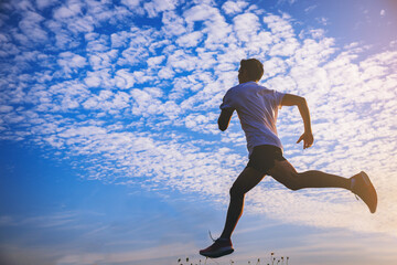 Silhouette of young man running sprinting on road. Fit runner fitness runner during outdoor workout with blue sky as background.