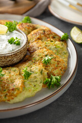 Zucchini pancakes with herbs and sour cream on a plate close-up vertical photo. Vegetarian dish