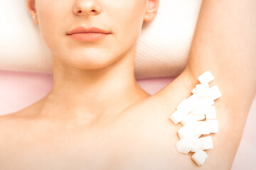 Obraz na płótnie Canvas Sugaring, waxing concept. White sugar cubes lie down on the female armpit of the young white woman, close up